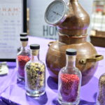 A small copper still with various botanicals in bottles
